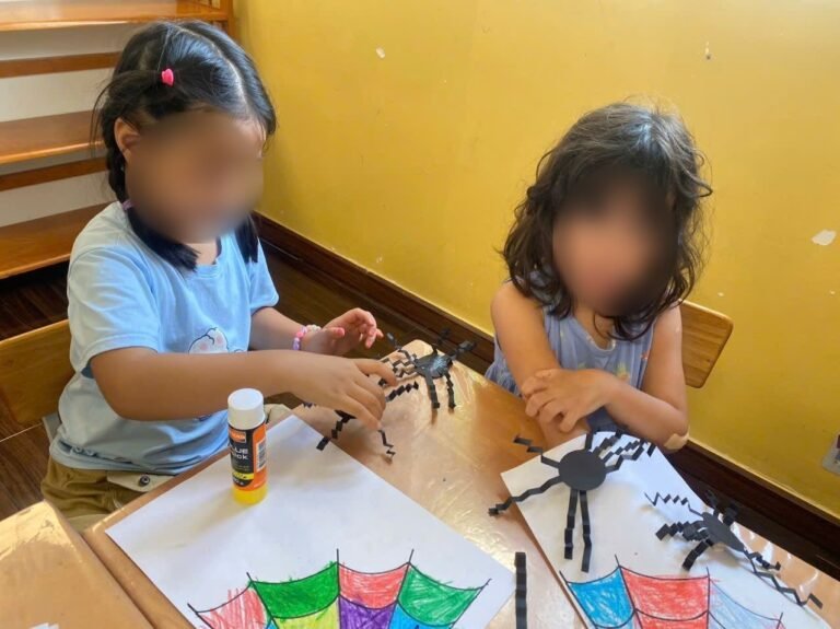 Two girls make paper spiders on colored-in webs