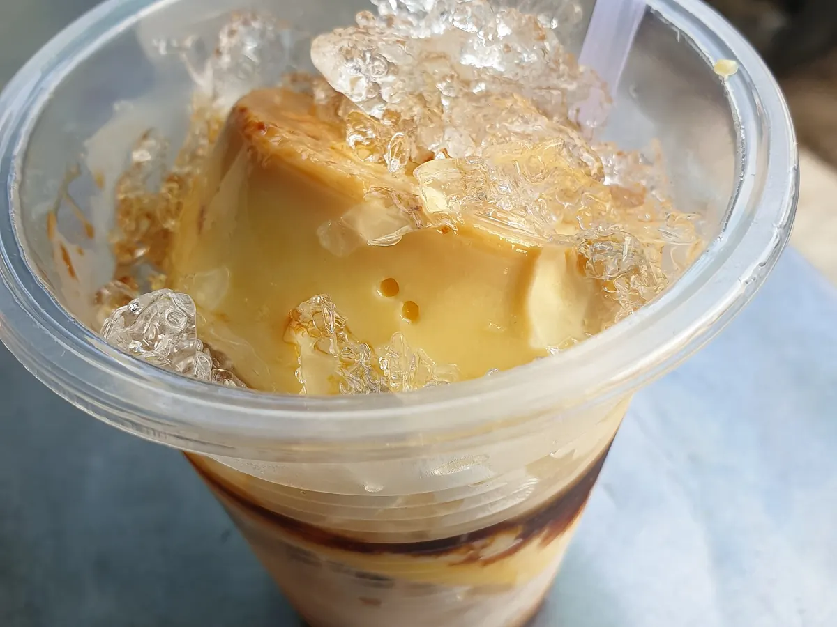 Un bánh flan servi dans un gobelet sur de la glace pilée, avec un fond de café