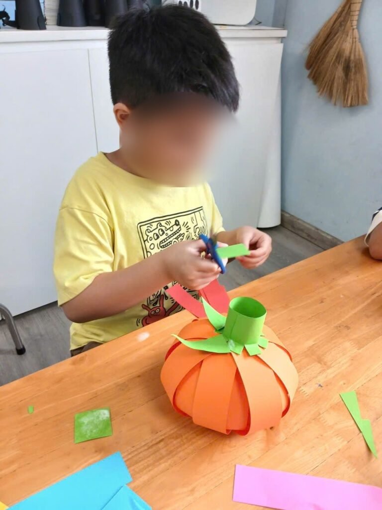 A boy puts together a pumpkin made of orange paper strips
