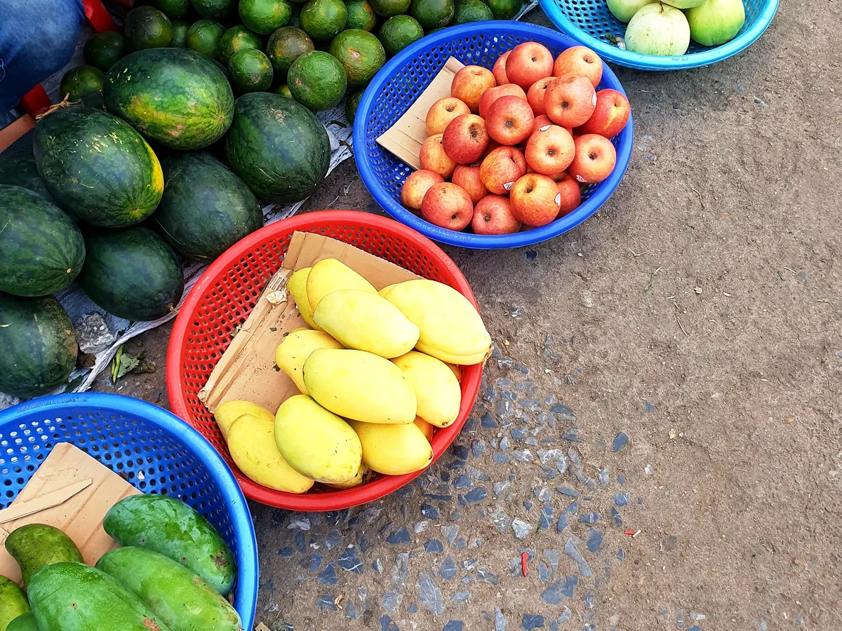 Un étal de fruits posé au sol dans un marché vietnamien : citrons verts, pastèques, pommes, mangues et papayes
