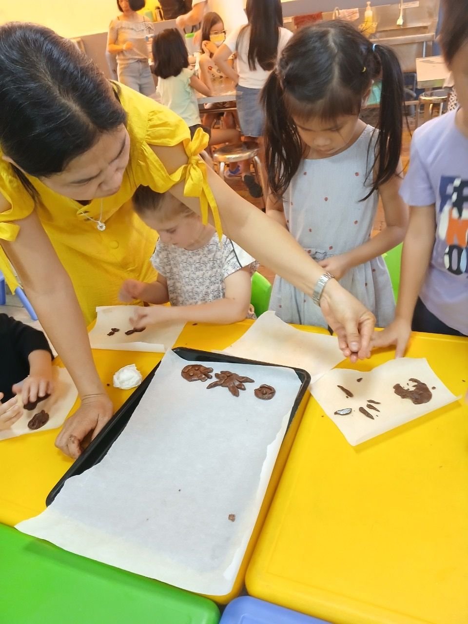 A woman from the team guides children as they shape cookies on a baking tray