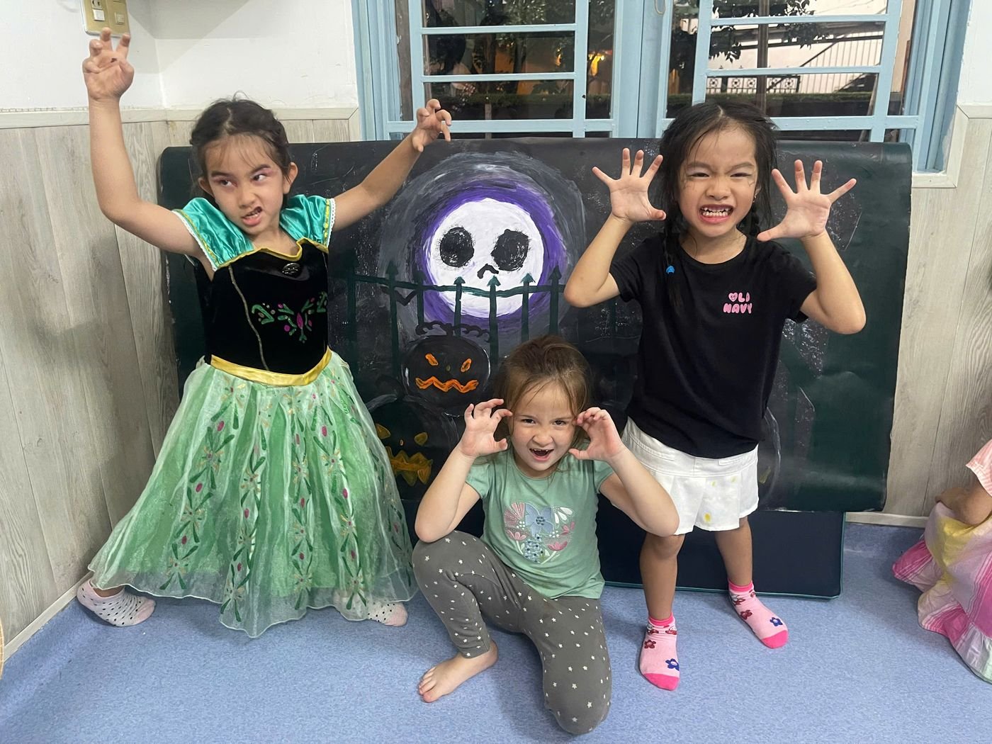 Four children in costume pretend to be monsters in front of a painted Halloween backdrop