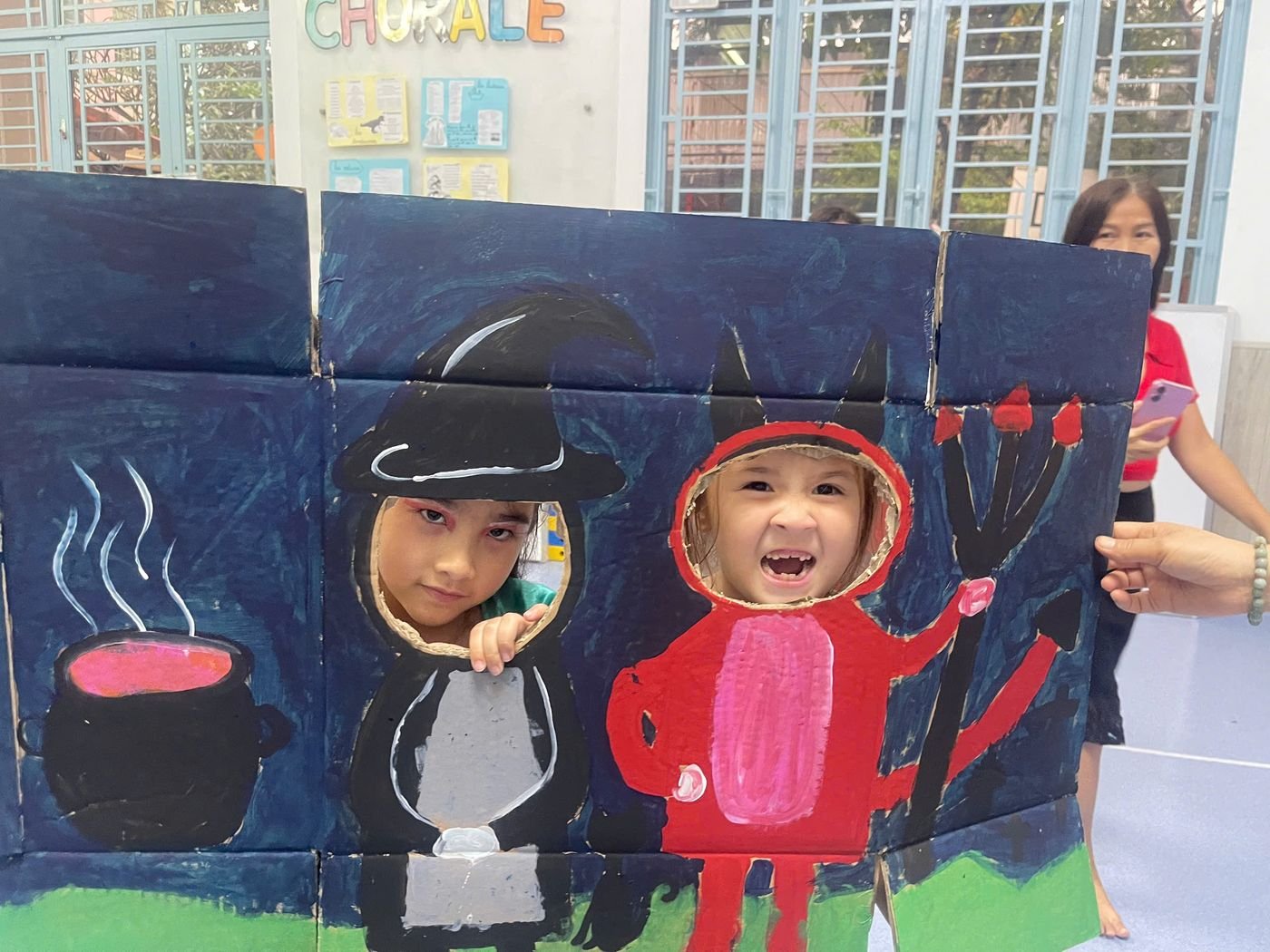 Two children poke their heads through a painted witch and devil photo board