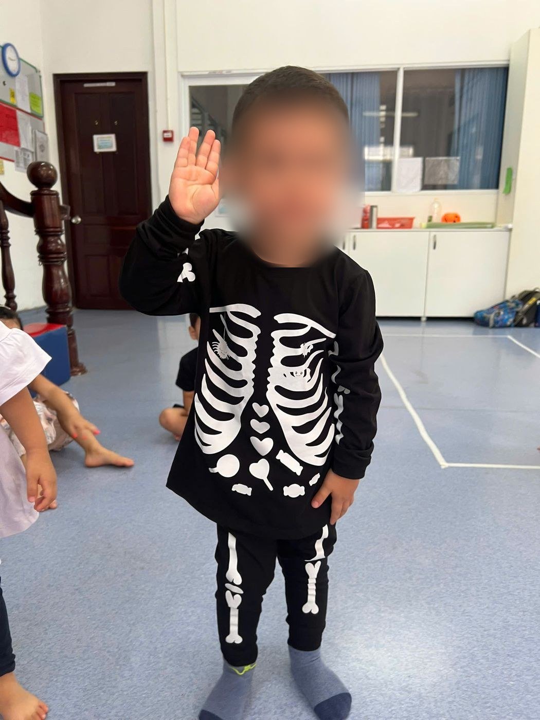 A little boy in a skeleton costume waves hello