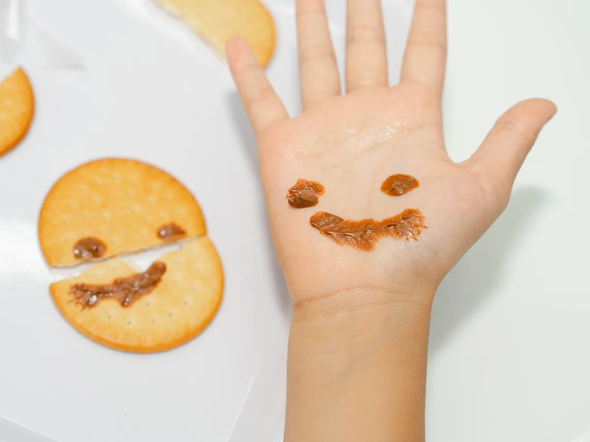 Une main d'enfant décorée d'un smiley en chocolat, à côté d'un biscuit décoré du même smiley