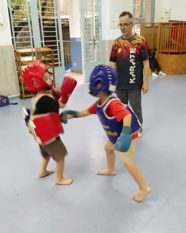 Deux enfants protégés par un casque et un plastron s'exercent au karaté sous l'œil de leur professeur, à Boule et Billes