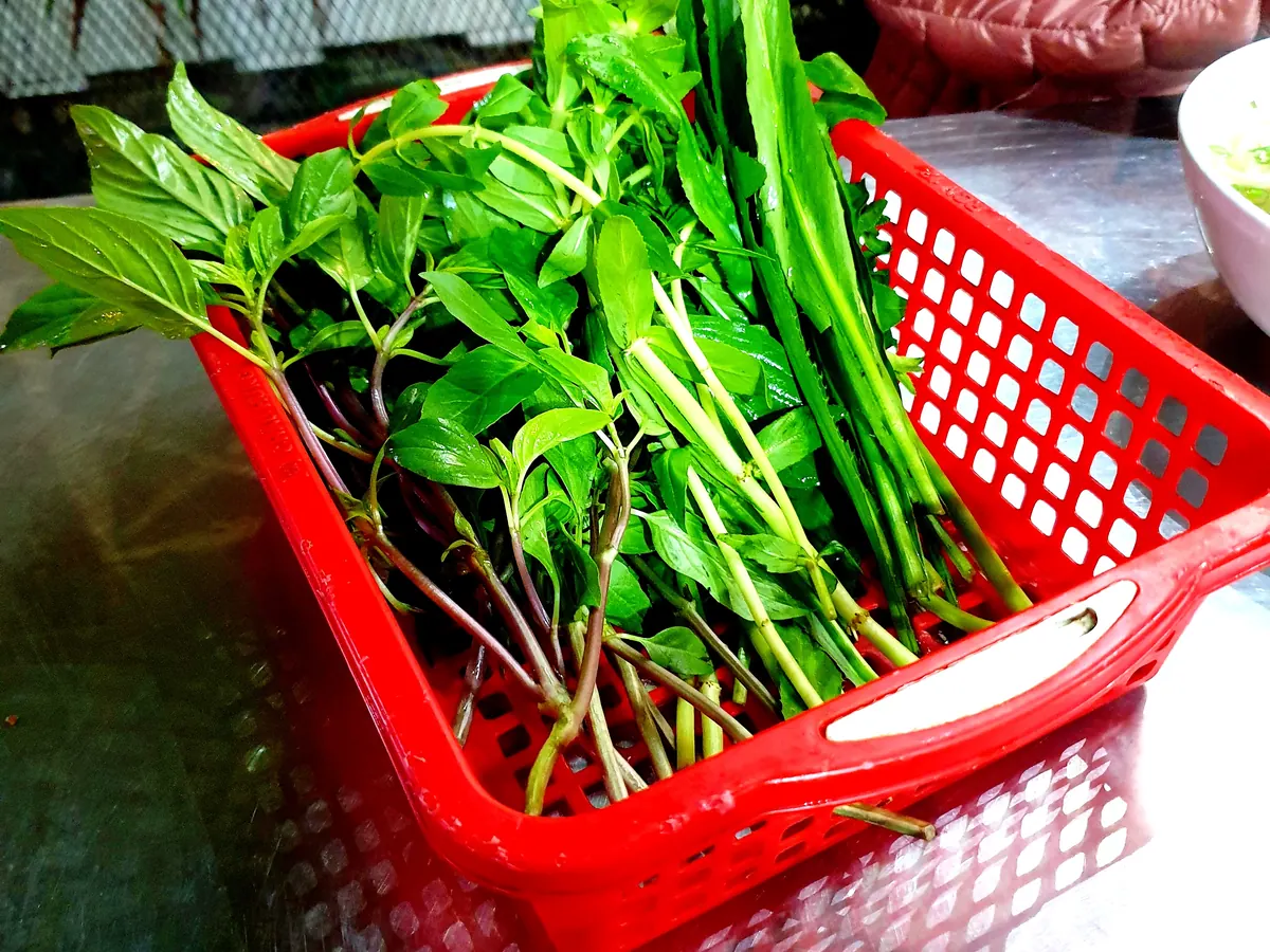 Un panier d'herbes fraîches servi avec un phở dans un restaurant de Thảo Điền