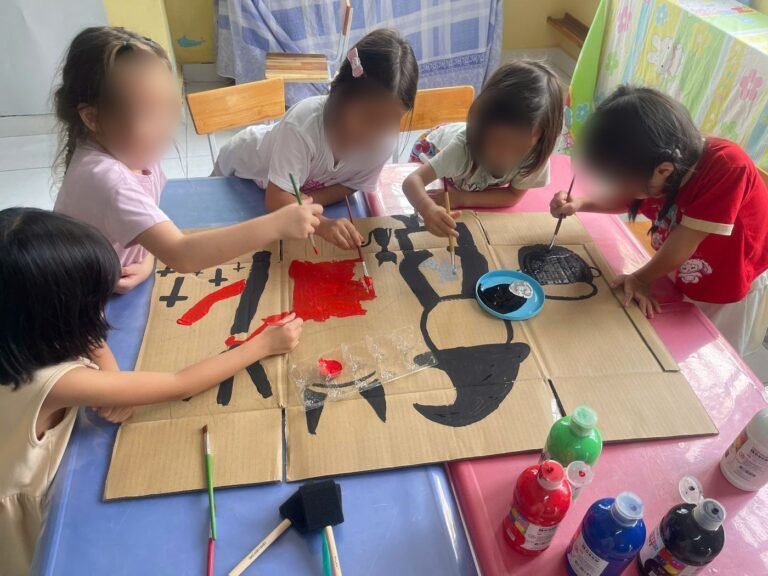 Four girls paint a witch together on a large piece of cardboard