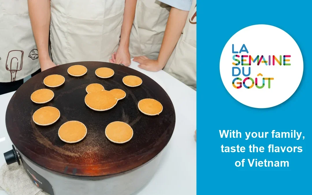 Crêpes cooking on a griddle at the Francophone Taste Games, one of them shaped like a mouse, next to the Semaine du goût logo and the words “With your family, taste the flavors of Vietnam”