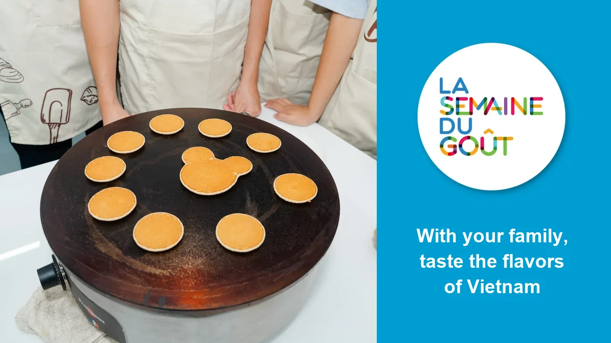 Crêpes cooking on a griddle at the Francophone Taste Games, one of them shaped like a mouse, next to the Semaine du goût logo and the words “With your family, taste the flavors of Vietnam”